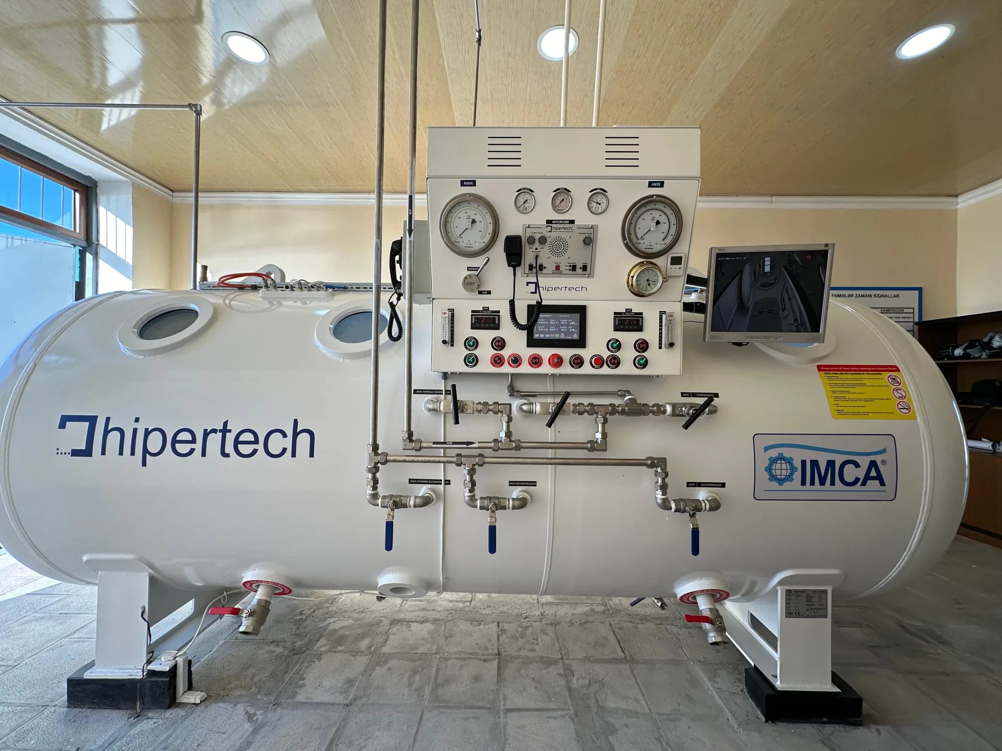 A delivered Hipertech twin-lock decompression chamber in its chamber room, the IMCA member decal on the hull beside the operating console